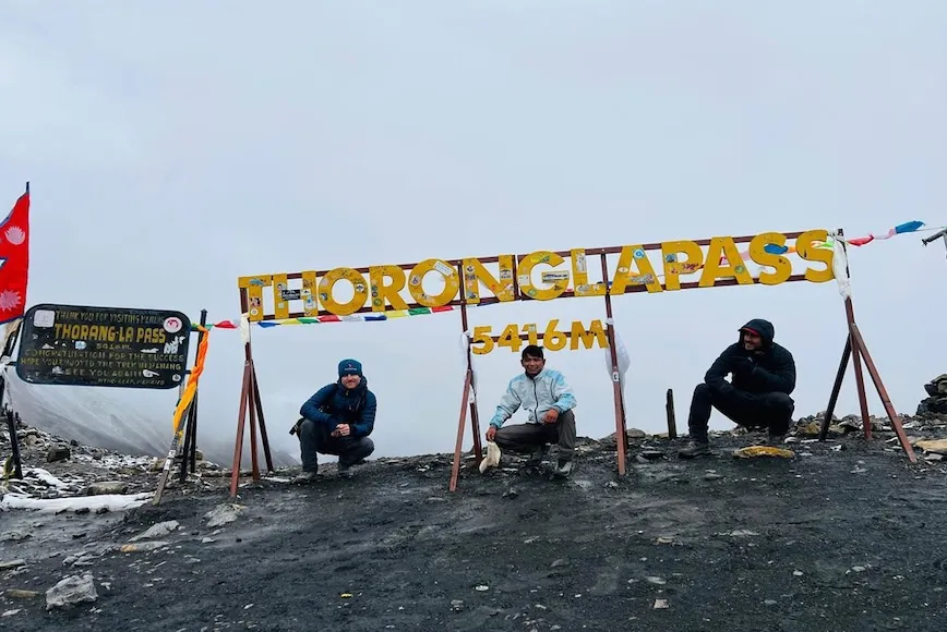Trekker standing beside the Thorong La Pass information board at 5,416 meters during the Annapurna Circuit Trek in Nepal